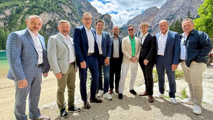 Nell’autunno 2022 il primo convegno sulle costruzioni massicce Nove uomini in abiti formali davanti a un lago di montagna con rocce sullo sfondo