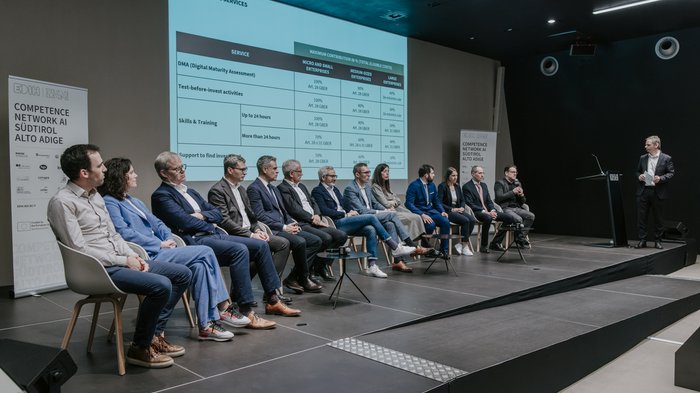 Anlaufstelle für Künstliche Intelligenz vorgestellt Podiumsdiskussion mit mehreren Personen auf der Bühne und Finanzierungsinformationen im Hintergrund