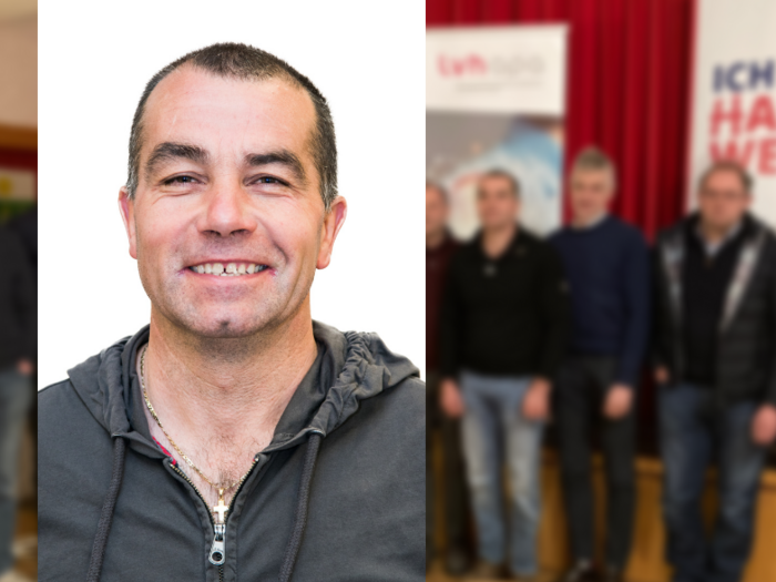 Fokus auf Photovoltaik Lächelnder Mann im Vordergrund, Gruppe von Männern vor Handwerksplakat im Hintergrund