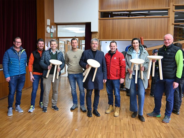 Handwerk zum Anfassen – 29. Tag des Handwerks in Jenesien Gruppe von Menschen hält selbstgemachte hölzerne drei-beinige Hocker im Raum