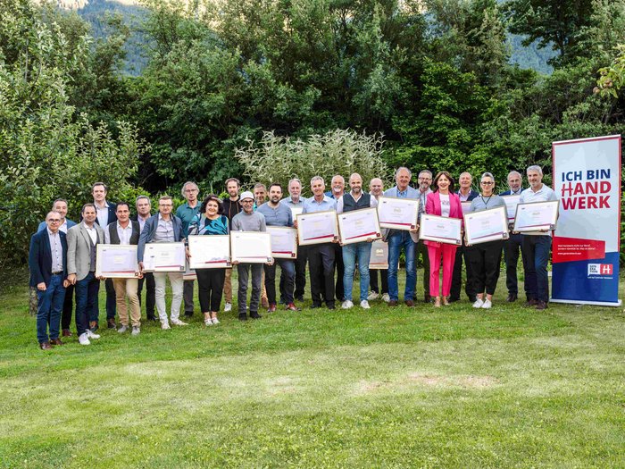 Consegna della spilla d’oro di lvh.apa Foto di gruppo di persone con certificati davanti a un banner Ich bin Handwerk all'aperto