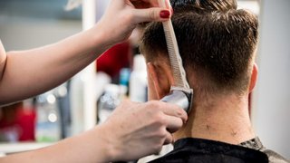 News Friseur schneidet Männern die Haare mit Haarschneidemaschine und Kamm