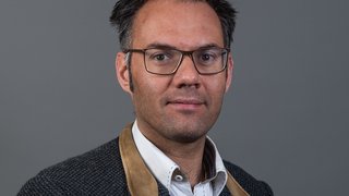 News Porträt eines Mannes mit Brille vor grauem Hintergrund