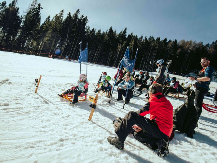 lvh Wintersportfest in Feldthurns Kinder und Erwachsene beim Rodelrennen auf verschneiter Piste mit Wald im Hintergrund