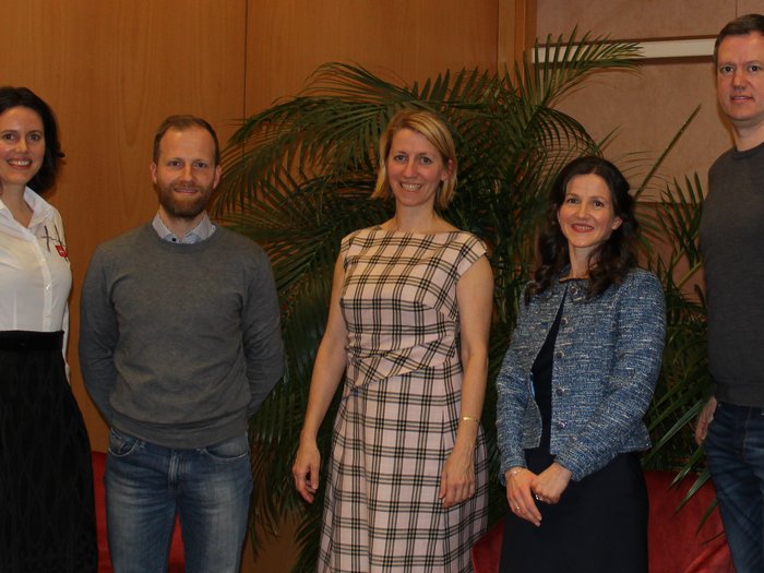 Assemblea annuale dei sarti su misura di lvh.apa Cinque persone in piedi davanti a piante e poltrone rosse in una stanza interna