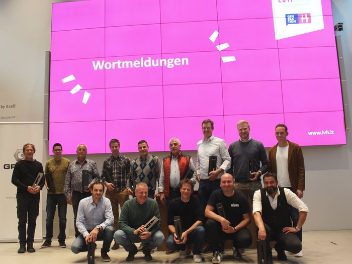 Richtpreisverzeichnis und Künstliche Intelligenz (KI) im Fokus Gruppenfoto von Männern vor einer großen rosa Leinwand mit dem Wort Wortmeldungen