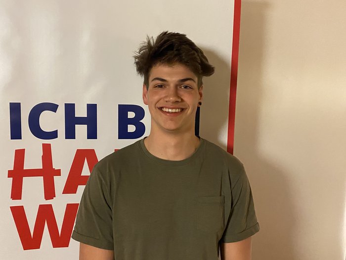 Auf jung folgt jung Junger Mann lächelt vor einem weißen Banner mit rotem und blauem Text