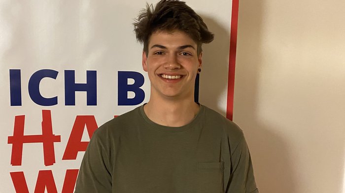 Auf jung folgt jung Junger Mann lächelt vor einem weißen Banner mit rotem und blauem Text