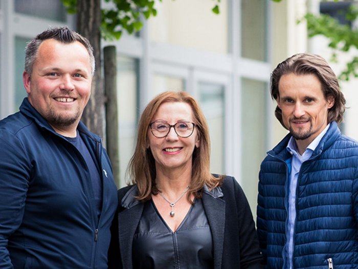 Medien, Design & IT: Die Qualität bildet den entscheidenden Unterschied Drei lächelnde Personen stehen vor einem Gebäude im Freien