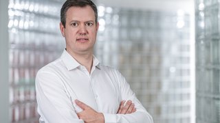 News Mann in weißem Hemd mit verschränkten Armen vor hellem Hintergrund