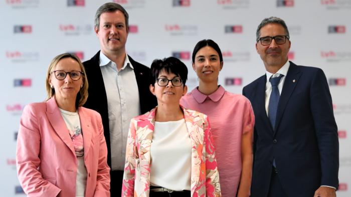 Bürokratie - weniger ist mehr! Fünf Personen formell und in pinkfarbenen Outfits vor Lvhb-Hintergrund