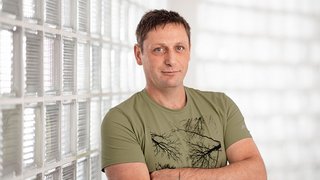 News Mann in grünem T-Shirt lehnt an Wand aus Glasbausteinen