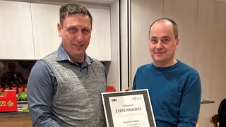 News Zwei Männer halten eine gerahmte silberne Ehrennadel Auszeichnung.