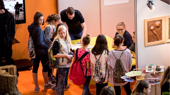 Talentcenter: Wegweiser für kluge Köpfe und geschickte Hände Gruppe von Jugendlichen an einem Messestand mit Ausstellern im Gespräch