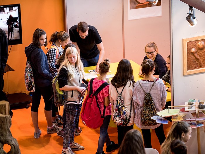 Talentcenter: Wegweiser für kluge Köpfe und geschickte Hände Gruppe von Jugendlichen an einem Messestand mit Ausstellern im Gespräch