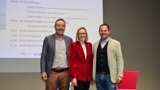 News Drei Personen vor Projektionsleinwand bei einer Veranstaltung mit Programm auf Deutsch