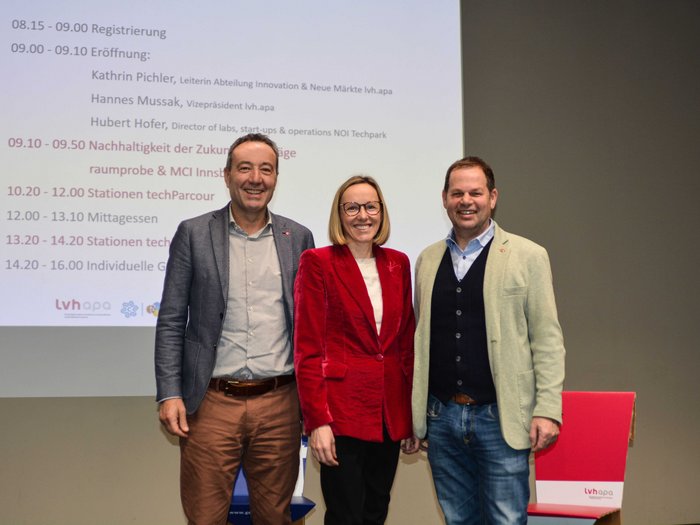 Der techParcour: Zukunft ist jetzt Drei Personen vor Projektionsleinwand bei einer Veranstaltung mit Programm auf Deutsch