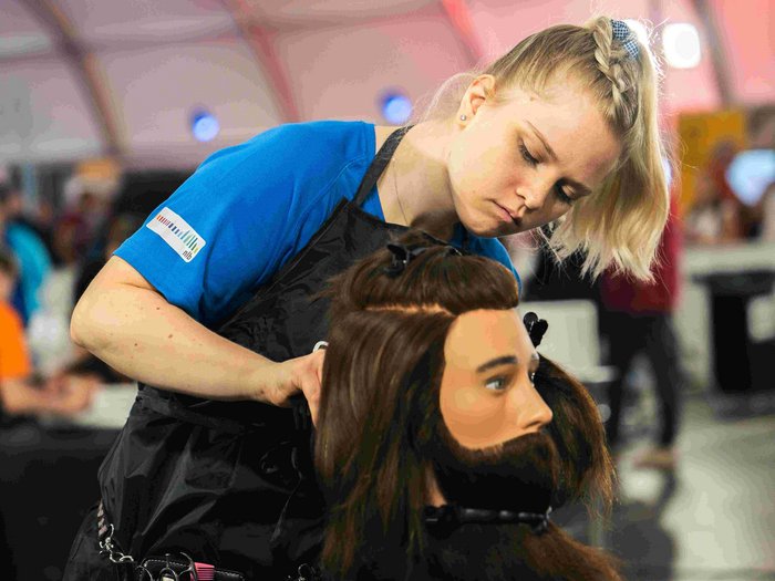 EuroSkills 2023: adesso bisogna concentrarsi! Parrucchiera che acconcia con concentrazione una testa di manichino maschile con capelli lunghi e barba