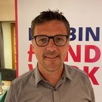 Klausen Porträt eines Mannes mit Brille vor Werbeplakat