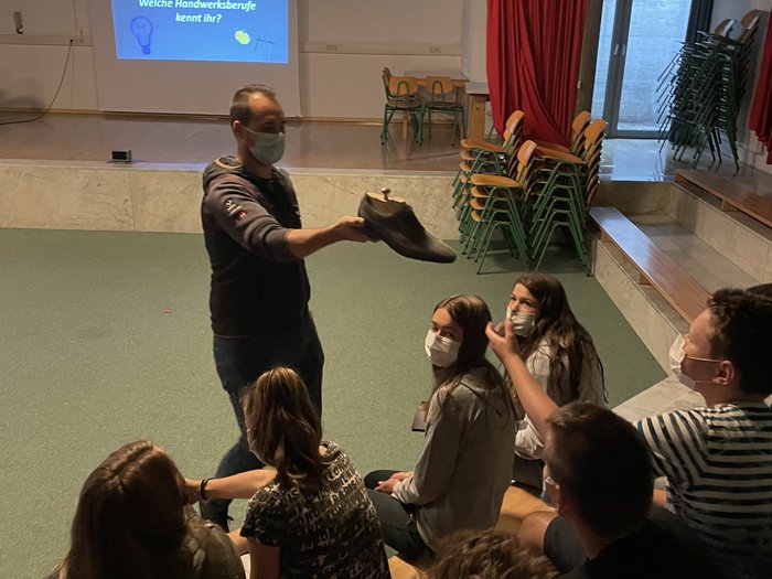 Berufe hautnah erleben Mann zeigt eine Schuhform vor sitzenden Jugendlichen in einer Unterrichtsumgebung