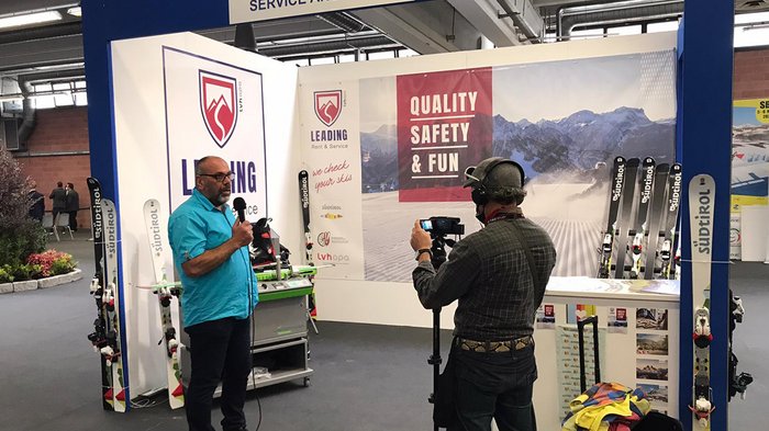 Sportgerätetechniker: Erstmals bei der Messe „Skipass 2021“ dabei Mann mit Mikrofon wird an einem Messestand für Skiservice gefilmt