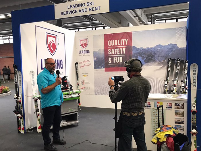 I tecnici per la manutenzione degli articoli sportivi protagonisti per la prima volta alla fiera “Skipass 2021” di Modena Uomo con microfono ripreso in uno stand fieristico di servizio sci