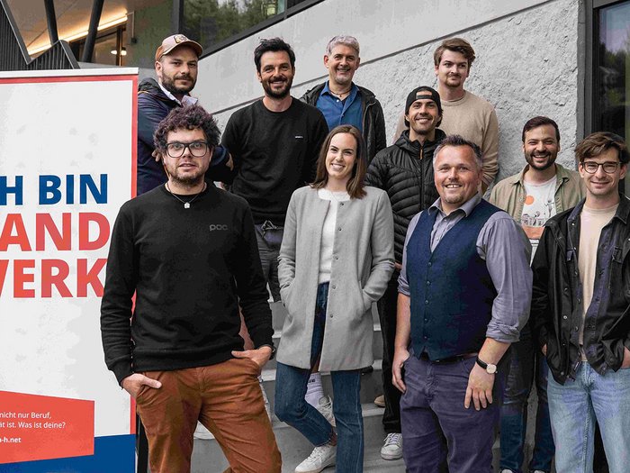 Die Berufsgemeinschaft hielt ihre Jahresversammlung auf dem Trainingsgelände des FC Südtirol ab. Hannes Fischnaller, Manager des Fußballklubs, lud alle Fotografinnen und Fotografen im lvh zu einer interessanten Führung ein. Gruppe von zehn Personen vor einem Schild mit Ich bin Handwerk