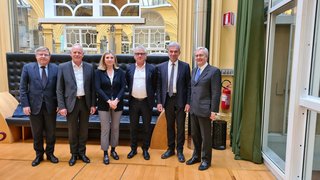 News Sechs Personen in Businesskleidung stehen in einem hellen Raum mit gelben Wänden