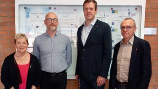 News Vier Personen stehen vor einer Wand mit Auszeichnungen und Urkunden