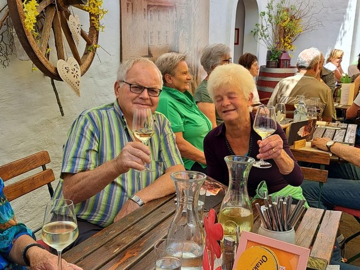 Viaggio culturale nel Burgenland – Opera e musical come fulcro del programma Anziani che brindano con vino a un tavolo di legno in un ristorante all'aperto soleggiato