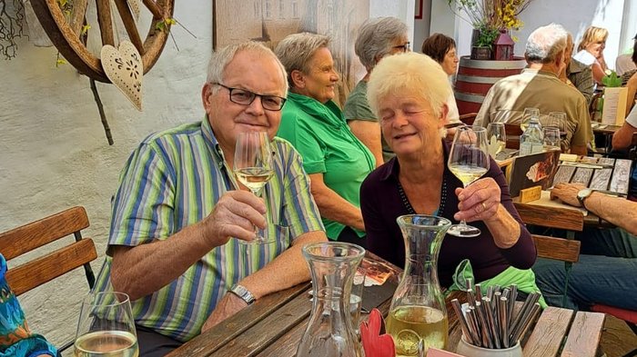 Viaggio culturale nel Burgenland – Opera e musical come fulcro del programma Anziani che brindano con vino a un tavolo di legno in un ristorante all'aperto soleggiato