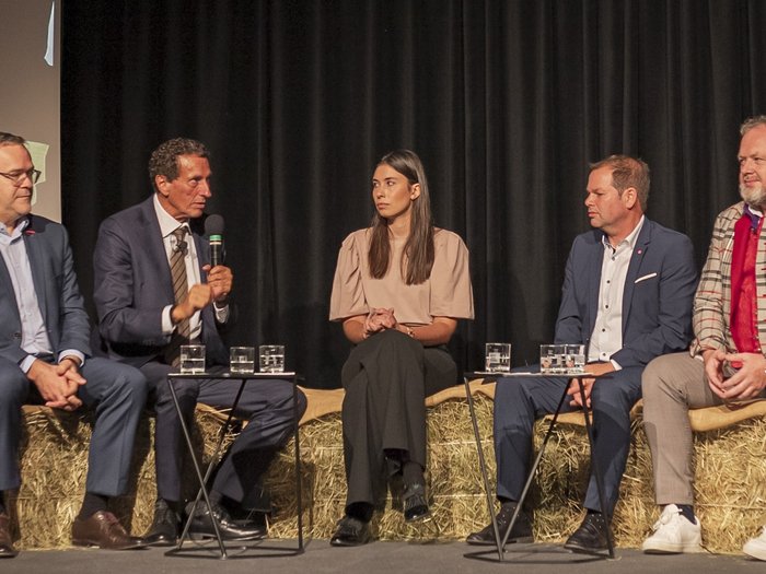 Giornata dell’Artigianato – I giovani come chiave di volta per il nostro futuro Cinque persone discutono durante un evento, sedute su balle di paglia con microfono