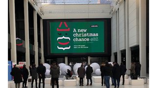 News Menschen stehen vor einer großen Leinwand mit Weihnachtswerbung in einem hellen Raum