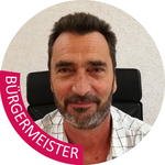 Burggrafenamt Porträt eines lächelnden Mannes mit Bart vor weißer Wand und Stuhl