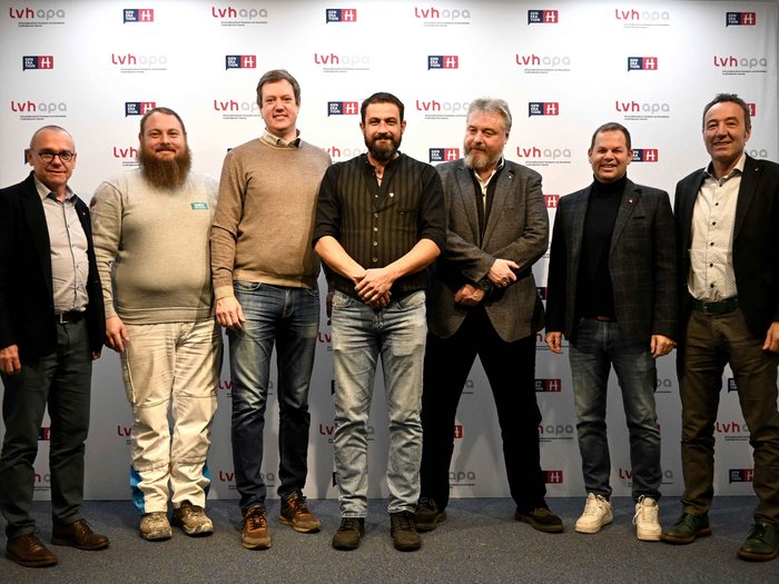 Erster Austausch mit Landtagsabgeordnetem Sieben Männer stehen vor einer lvh apa und Generation H Wand für ein Gruppenfoto