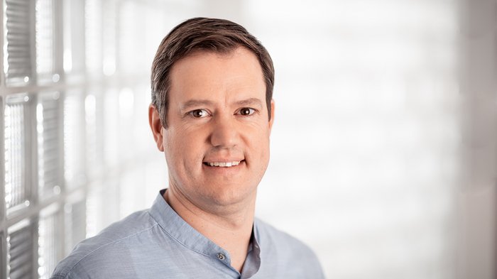 Haller: „Jetzt ist Zusammenhalt gefragt“ Porträt eines lächelnden Mannes mit blauem Hemd vor hellem Hintergrund