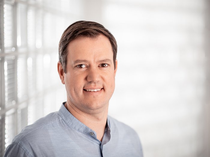 Haller: „Jetzt ist Zusammenhalt gefragt“ Porträt eines lächelnden Mannes mit blauem Hemd vor hellem Hintergrund