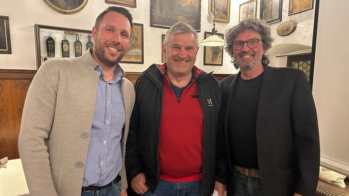 Weichenstellung für die Zukunft und Ehrung eines verdienten Handwerkers Drei Männer stehen lächelnd in einem Raum mit Bildern an der Wand