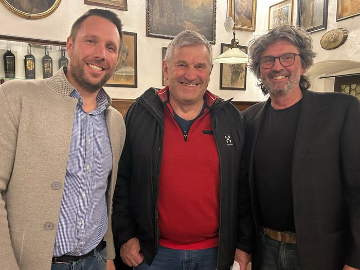 Weichenstellung für die Zukunft und Ehrung eines verdienten Handwerkers Drei Männer stehen lächelnd in einem Raum mit Bildern an der Wand