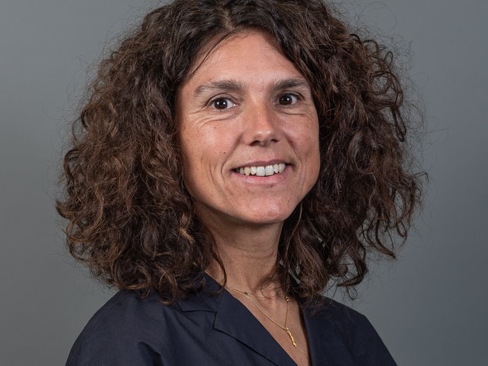 Altreifenentsorgung Porträt einer lächelnden Frau mit lockigem braunem Haar vor grauem Hintergrund