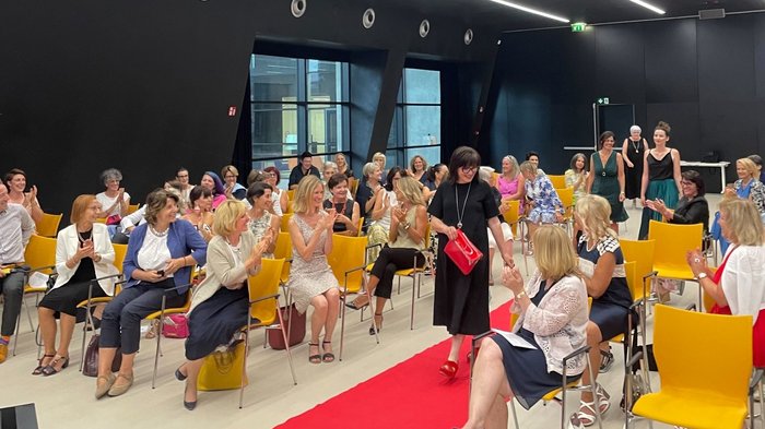 Spannung bei der Präsentation des Umstylings © lvh.apa Frau läuft auf rotem Teppich vor applaudierendem Publikum in modernem Raum