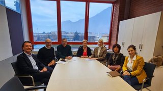 News Gruppo di sette persone sedute intorno a un tavolo in una riunione in ufficio con grande finestra