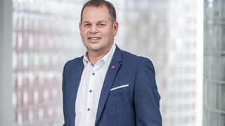 News Mann in blauem Anzug vor Glasbausteinwand lächelnd