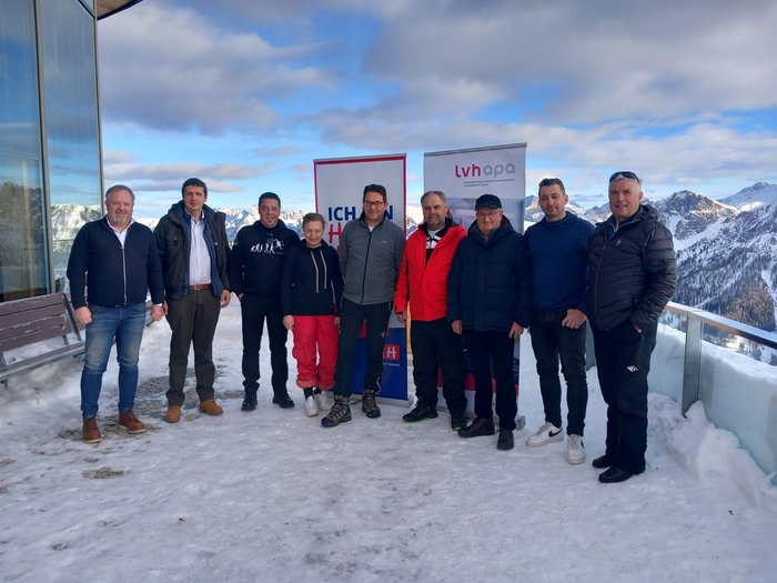 Treffen über den Wolken Gruppe von zehn Personen steht auf schneebedecktem Balkon mit Bergen im Hintergrund