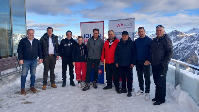 Treffen über den Wolken Gruppe von zehn Personen steht auf schneebedecktem Balkon mit Bergen im Hintergrund