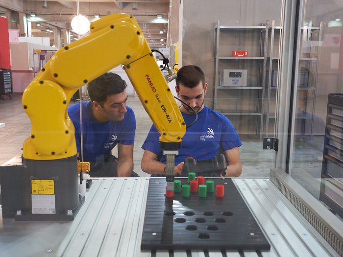 WorldSkills Italy: Obiettivo Lione Due uomini controllano un braccio robotico giallo in un'officina