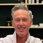 Oberpustertal Mann mit grauen Haaren und weißem Hemd lächelt vor Regal