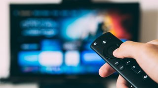 News Hand hält Fernbedienung vor Fernseher mit Streaming-App-Benutzeroberfläche