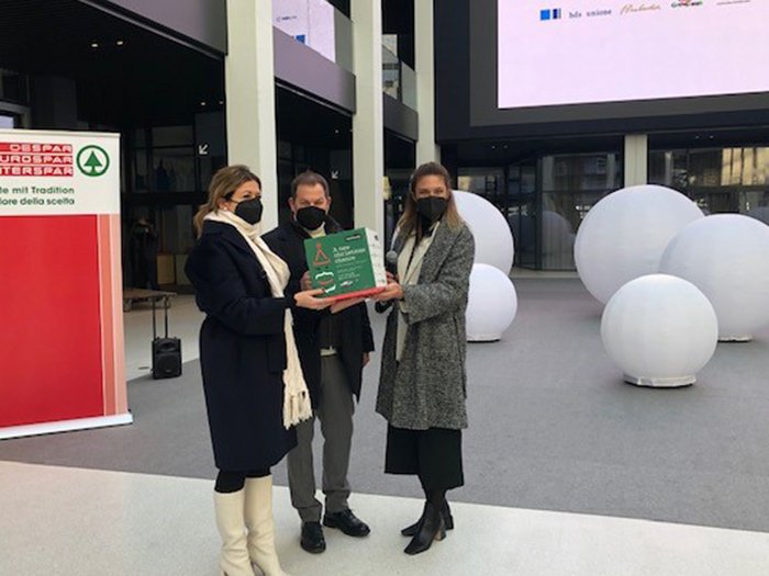 A NEW CHRISTMAS CHANCE: ES GEHT LOS! Drei Personen mit Masken halten zusammen eine grüne Box in einem modernen Innenraum