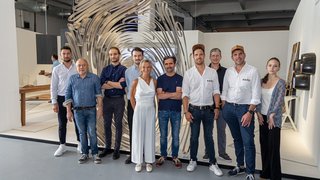 News Gruppe von elf Personen vor einer großen abstrakten Skulptur in einem Innenraum